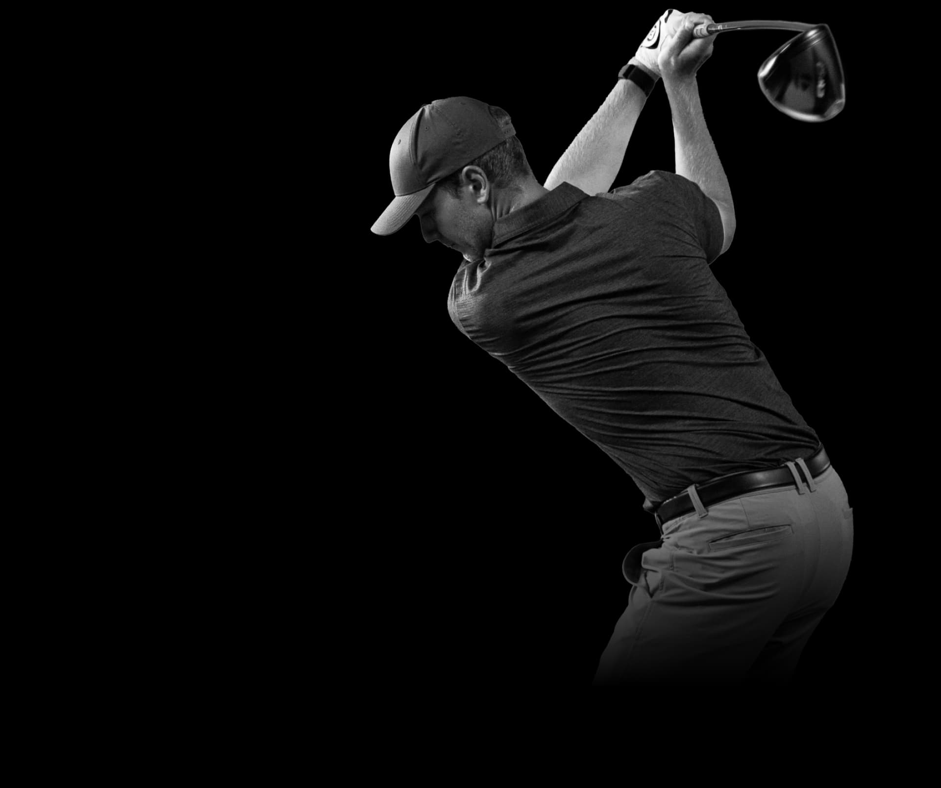Golfer in mid-swing, wearing a cap and polo shirt, holding a driver, with a focused posture against a plain background.